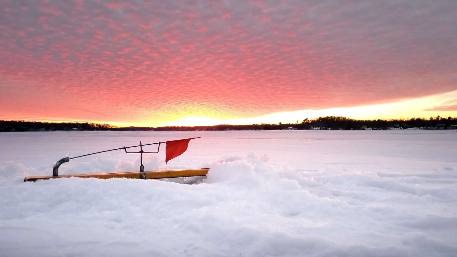 Sunset over a pond with an ice fishing hole